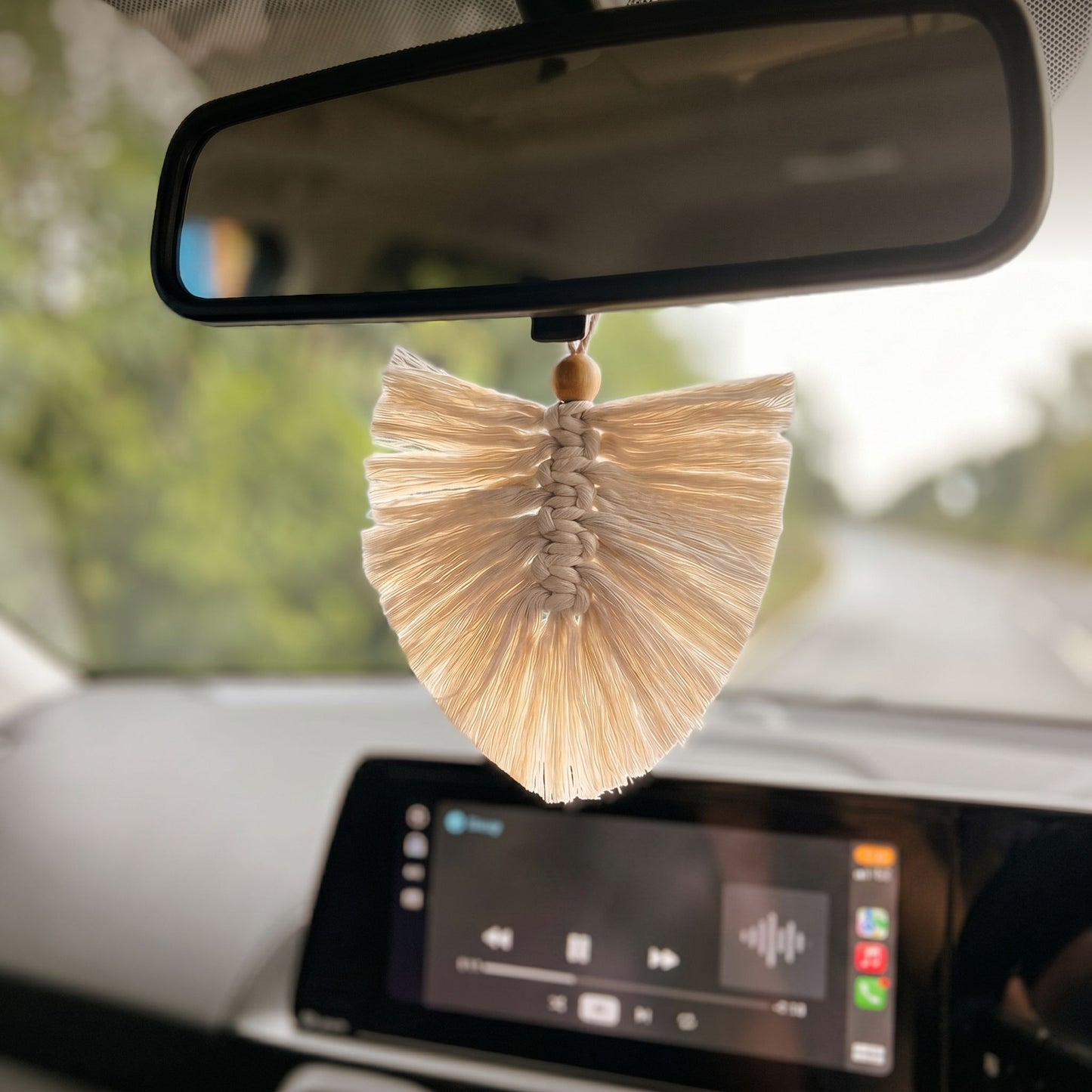 Decorative car feather hanging on a car's rearview mirror with a blurred natural background
